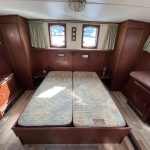 Photo de la cabine arrière du bateau. On y voit au centre le lit double composé de deux matelas pour lit simple et sur les côtés des rangements dans des commodes en bois.