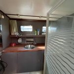 Image de la salle de bain du bateau avec à gauche la douche et au centre un grand meuble avec un lavabo au milieu.