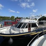 Vue d'ensemble du bateau WHY NOT. Sa coque est bleu foncé avec une bande jaune au-dessus.