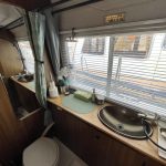 Photo de la salle de bain du bateau. Elle est équipée d'une douche, d'un évier et d'un toilette. Les meubles sont en bois et le sol est blanc.